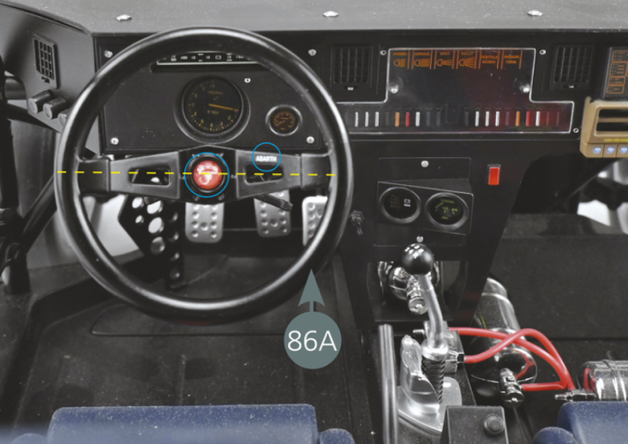Take the front frame assembly made in stage 86 and align it with the seating unit. Tilt the lower frame (5A) (as indicated by the red arrow) and place the left and right floorboards (67A & 67B) on top (yellow arrows). Ensure that the clutch pedal (20B) is in front of the left front roll bar bracket (89C), as indicated by the blue circle and arrow.