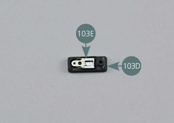 Place the door handle support (103D) with the inside facing up – see picture. Insert the door handle (103E) into the housing, ensuring that the pin is correctly aligned with the opening (yellow circle). The door handle is assembled upside down.