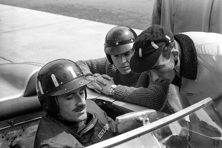 El inglés Graham Hill, en el Porsche 718 WRS, hablando con Dan Gurney (centro), piloto del 718 GTR Coupé, y Stirling Moss (derecha) antes del inicio de los 1.000 km de Nürburgring de 1962. © IXO Collections SAS - Tous droits réservés. 