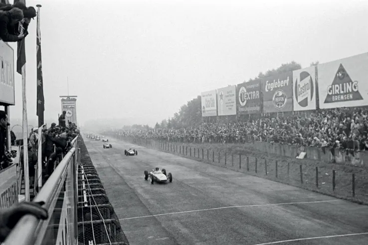 Im Vordergrund der Porsche 804 Nr. 7 von Dan Gurney beim Großen Preis von Deutschland, wo der amerikanische Fahrer in der Qualifikation die Pole Position errang, jedoch hinter Graham Hills BRM und John Surtees' Lola auf dem dritten Platz landete.© IXO Collections SAS - Tous droits réservés. 