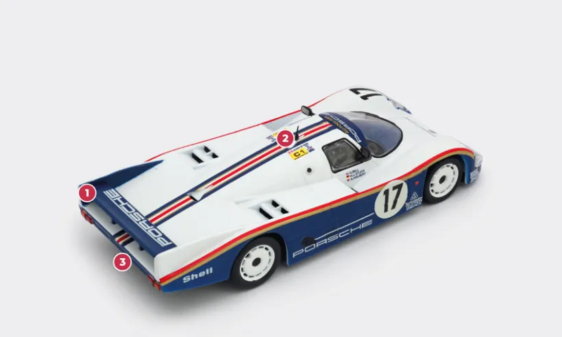 1. Like the 956, the 962 benefited for Le Mans from a special aerodynamic configuration adapted to the circuit, characterised by a rear bonnet of the same length but with a lower, horizontal spoiler to enhance top speed on the straights.2. The 3-litre engine producing nearly 800 bhp, which made its debut in 1987, was the second evolution of the original 2.65-litre twin-turbo boxer engine from the 965, first increased to 2.85 litres, then to 3 litres, and finally to 3.2 litres, but still as reliable as ever.3. The engine and gearbox serve as load-bearing elements. The gearbox, integrated with the engine, acts as a support for the upper suspension mountings.© IXO Collections SAS - Tous droits réservés.&nbsp;